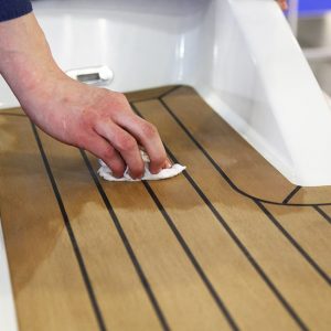 La mano di un uomo pulisce il ponte in legno di uno yacht usando un detergente