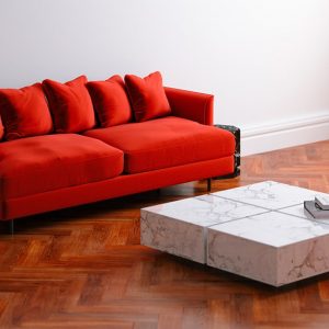 Salotto moderno e minimale con sofà rosso, tavolino da caffè in marmo e parquet in bubinga