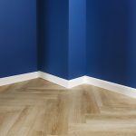 Dettaglio di una stanza con pareti blu, battiscopa in legno bianco e parquet chiaro