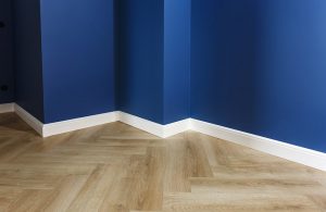 Dettaglio di una stanza con pareti blu, battiscopa in legno bianco e parquet chiaro