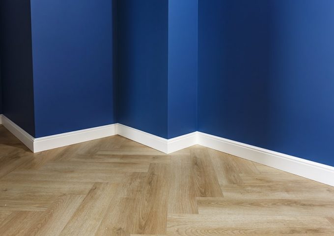 Dettaglio di una stanza con pareti blu, battiscopa in legno bianco e parquet chiaro