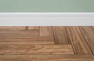 Dettaglio di un battiscopa bianco installato tra un muro verniciato di verde e un parquet a spina di pesce