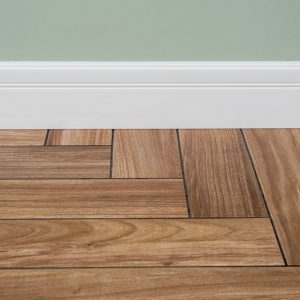 Dettaglio di un battiscopa bianco installato tra un muro verniciato di verde e un parquet a spina di pesce