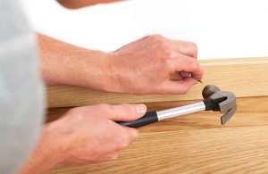 Un uomo sta installando un battiscopa in legno inchiodandolo al muro