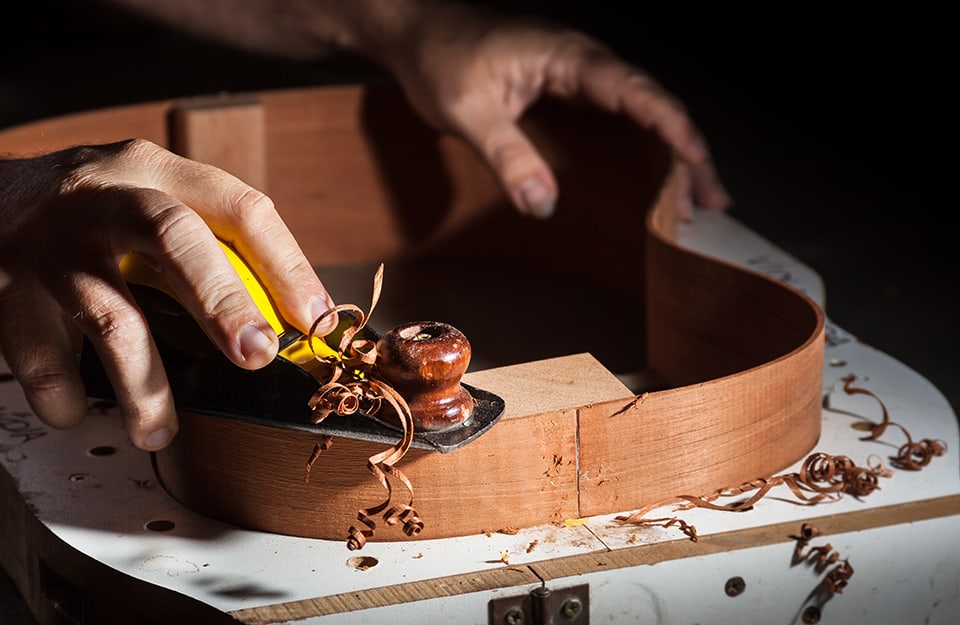 Primo piano di un liutaio che lavora al telaio di una chitarra in legno di palissandro