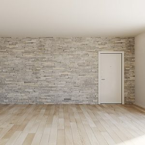 Stanza vuota con finestra da cui entra la luce, pareti e soffitto bianco e una parete con pietra a vista con porta bianca. Il parquet è in rovere chiaro