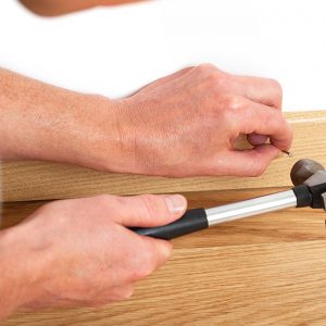 Un uomo sta installando un battiscopa in legno inchiodandolo al muro