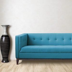 Salotto minimale con parquet in betulla, una finestra, un sofà trapuntato azzurro e un grande vaso nero e grigio dalle linee sinuose