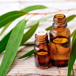 Due flaconcini di olio di eucalipto accanto ad alcune foglie della pianta, disposte su una superficie in legno