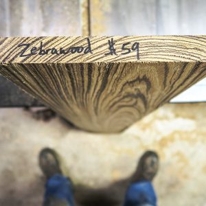 Vista dall'alto di un'asse di legno di zebrano in piedi davanti a un operaio di cui si vedono solo i piedi