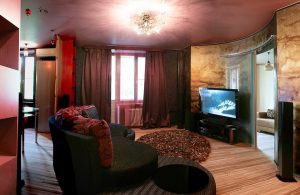Salotto sui toni del rosso con tv accesa e parquet in zebrano