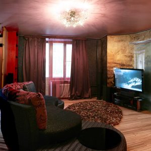 Salotto sui toni del rosso con tv accesa e parquet in zebrano