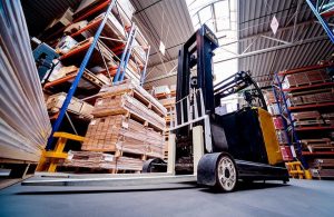 Un carrello elevatore visto dal basso, nel magazzino di un'industria di parquet piena di scaffali e pallet con assi di legno