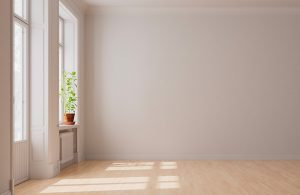Stanza vuota con parquet in betulla e, sulla sinistra, delle finestre aperte da cui entra luce, sul davanzale di una delle quale si vede una piantina in vaso