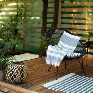 Salotto esterno sotto a una veranda con pavimento in decking, molte piante e fili di luci a LED