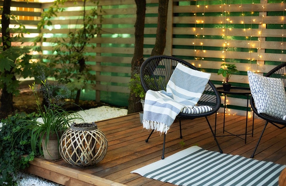 Salotto esterno sotto a una veranda con pavimento in decking, molte piante e fili di luci a LED
