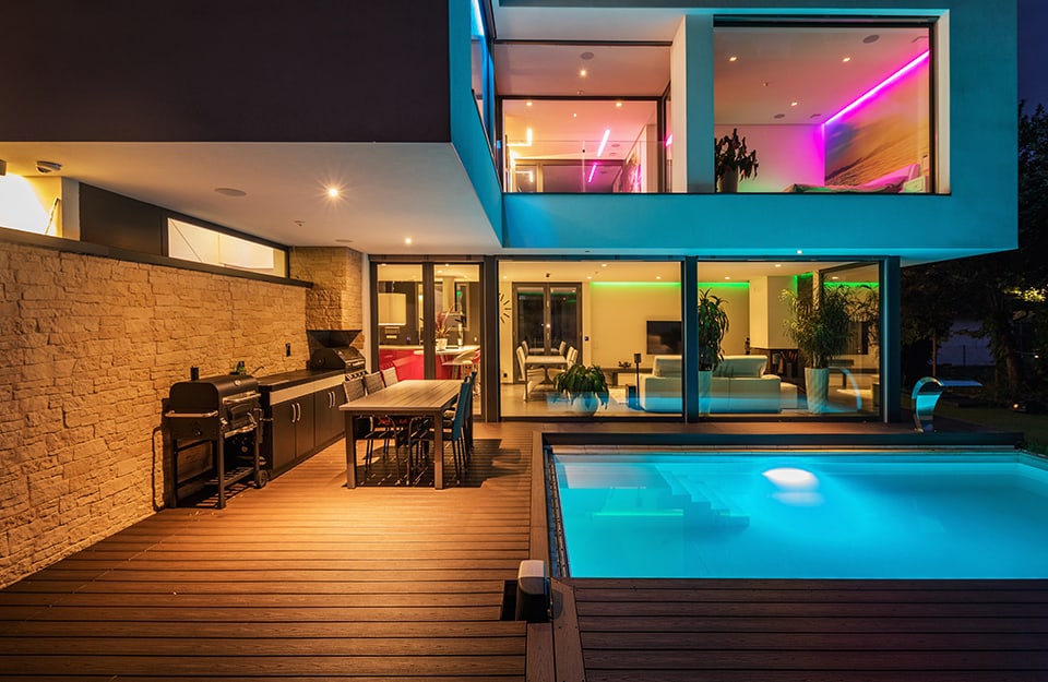 Grande villa modernista con piscina illuminata, stanze interne con luci colorate e decking esterno con cucina all'aperto