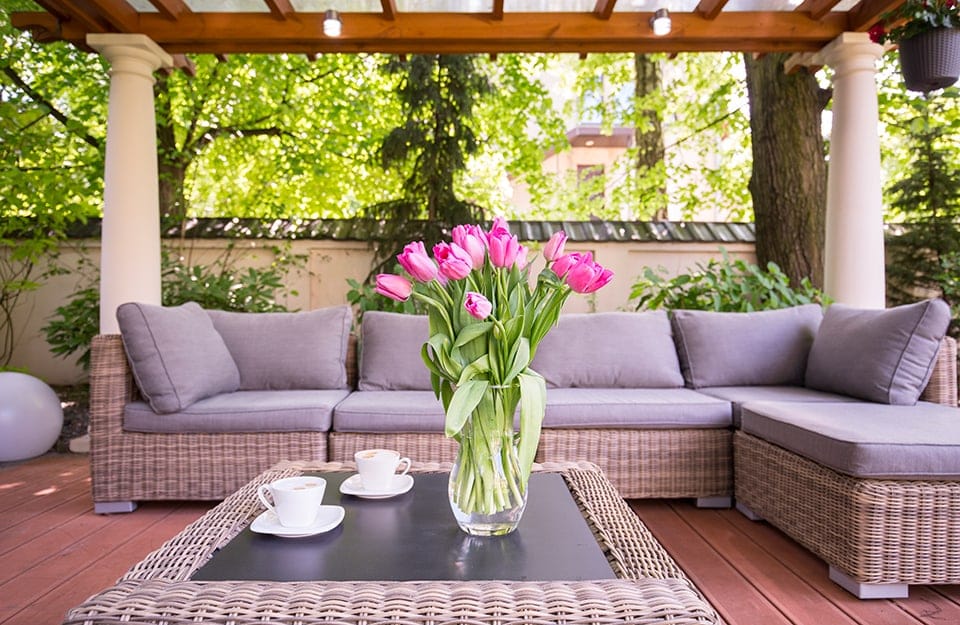 Salotto esterno in rattan sotto a un pergolato con colonne