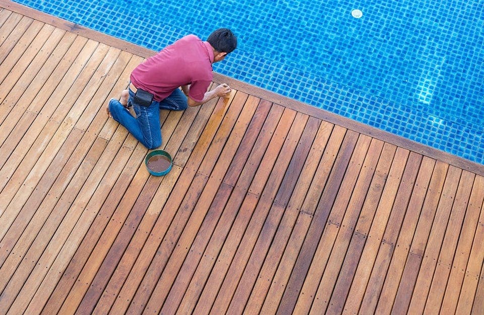 Uomo fa manutenzione al tavolato del decking accanto a una piscina