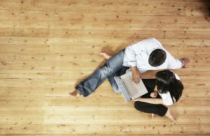 Una coppia guarda in un computer portatile seduta su un parquet in pino. La scena è vista dall'alto