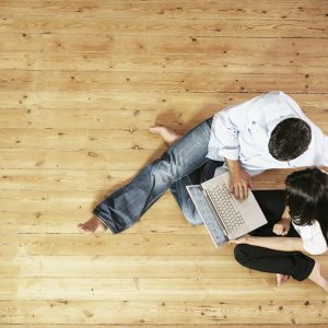 Una coppia guarda in un computer portatile seduta su un parquet in pino. La scena è vista dall'alto