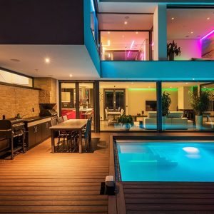 Grande villa modernista con piscina illuminata, stanze interne con luci colorate e decking esterno con cucina all'aperto