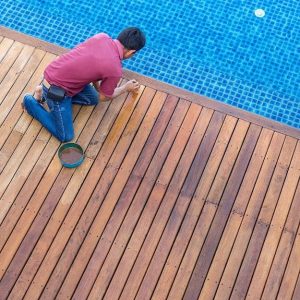 Uomo fa manutenzione al tavolato del decking accanto a una piscina