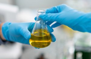 Due mani con guanti azzurri si passano una provetta con un liquido giallo in un laboratorio