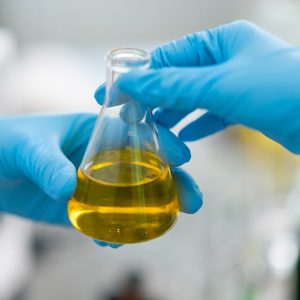 Due mani con guanti azzurri si passano una provetta con un liquido giallo in un laboratorio