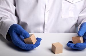 Uno scienziato con camice bianco e guanti blu maneggia dei piccoli cubi in legno