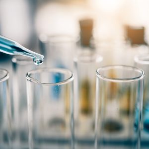 Delle provette in laboratorio con un contagocce che versa un liquido azzurro in una di esse