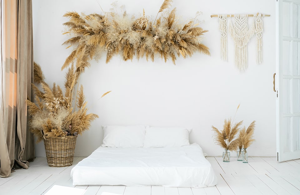 Una stanza da letto tutta sui toni del bianco e in stile Boho Chic, con materasso sul parquet e decorazioni con piante secche e vimini