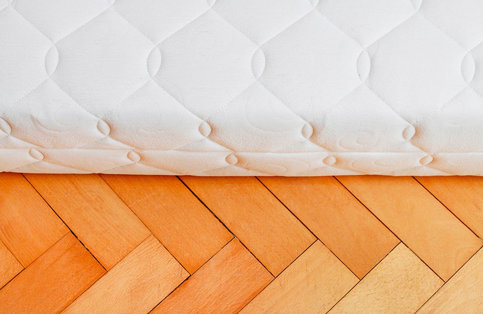 Dettaglio di un materasso poggiato su un parquet a spina di pesce