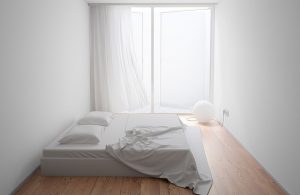 Piccola stanza da letto minimale con pareti e soffitto bianco, doppio materasso poggiato direttamente sul parquet, finestra aperta che occupa un'intera parete e lampada a globo poggiata sul pavimento