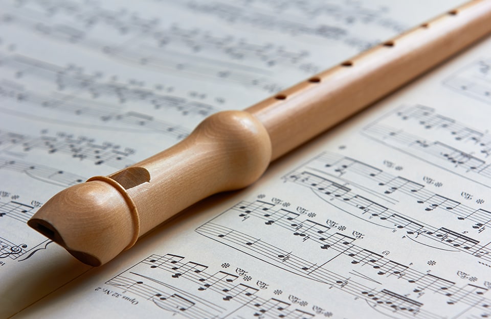 Un flauto in legno di pero poggiato sopra a uno spartito musicale
