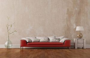 Salotto minimale con parquet in legno di pero, muro lasciato grezzo, grande sofà rosso, vaso in vetro con dentro il ramo di una pianta, tavolino con lampada