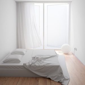 Piccola stanza da letto minimale con pareti e soffitto bianco, doppio materasso poggiato direttamente sul parquet, finestra aperta che occupa un'intera parete e lampada a globo poggiata sul pavimento
