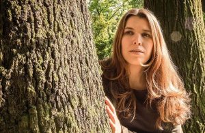 La cantautrice Erica Boschiero si affaccia da dietro un albero, in una foresta