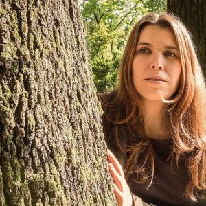 La cantautrice Erica Boschiero si affaccia da dietro un albero, in una foresta