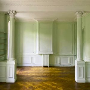 Un salone vuoto in un'antica casa con stucchi e colonne, e un pavimento in parquet da restaurare