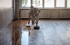 Un professionista della posa e del restauro del parquet applica una finitura a olio in una luminosa stanza con parquet a spina di pesce