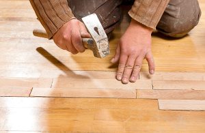 Un parquettista sta lavorando al restauro di un vecchio parquet con un martello in mano