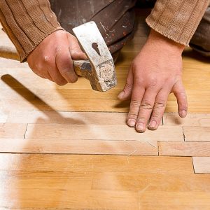 Un parquettista sta lavorando al restauro di un vecchio parquet con un martello in mano