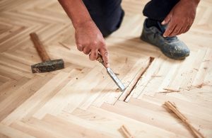 Un parquettista sta lavorando al restauro di un vecchio parquet con uno scalpello e un martello