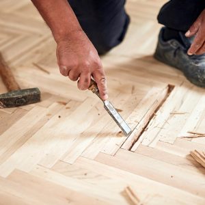 Un parquettista sta lavorando al restauro di un vecchio parquet con uno scalpello e un martello