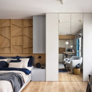 Camera da letto moderna con armadio con ante a specchio, pavimento in parquet, poltrona e letto con parete in boiserie dalle geometrie moderne