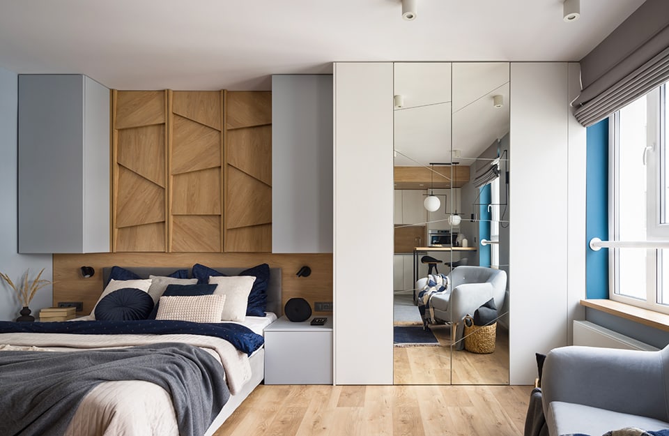Camera da letto moderna con armadio con ante a specchio, pavimento in parquet, poltrona e letto con parete in boiserie dalle geometrie moderne