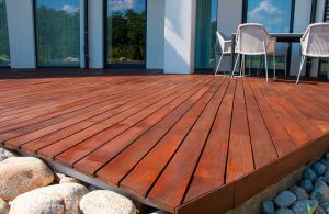 Dettaglio di un decking in legno di sucupira, con attorno grossi ciottoli bianchi e delle sedie sopra