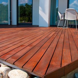 Dettaglio di un decking in legno di sucupira, con attorno grossi ciottoli bianchi e delle sedie sopra