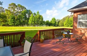 Giardino con decking in legno di sucupira, che ospira arredi da giardino e, attraverso una scala, dà su un grande prato verde delimitato, in fondo, da molti alberi